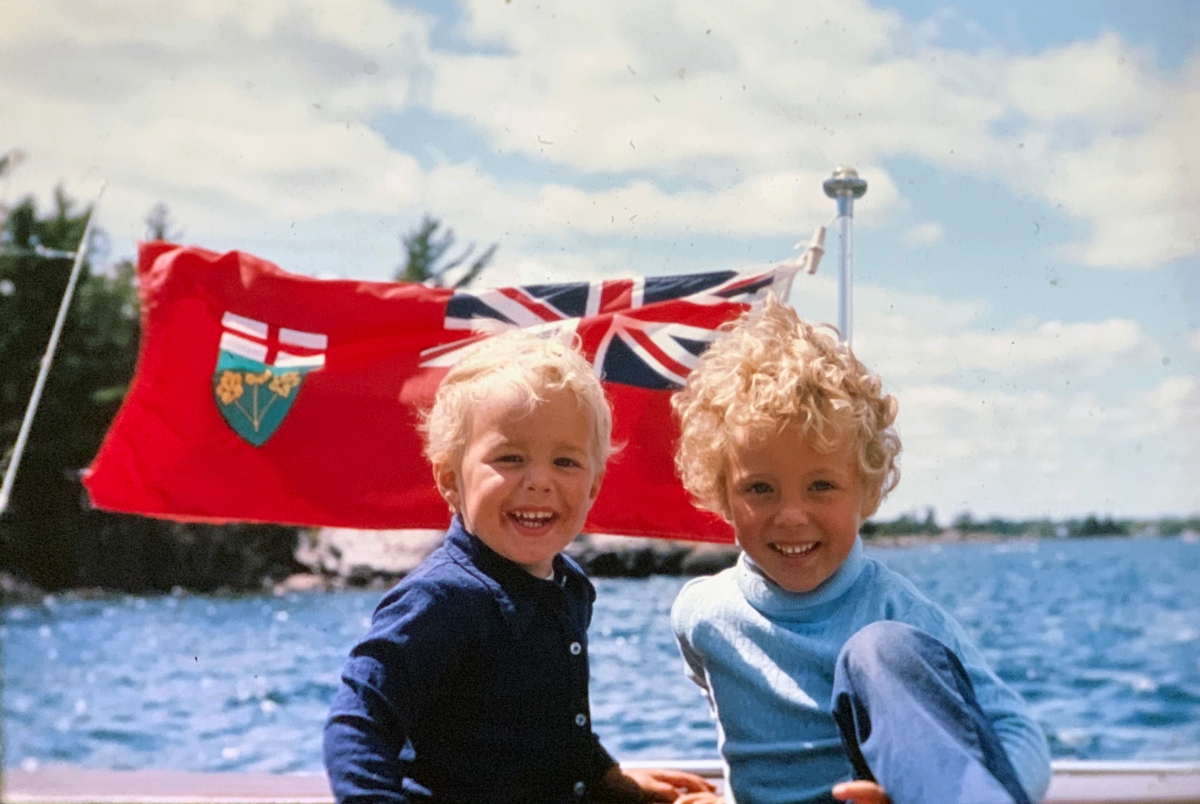 Two kids in a boat in front of the Ontario flag.